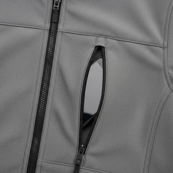 Closeup of a grey softshell jacket showing a black smartphone stored inside the angled, zippered Napoleon chest pocket.