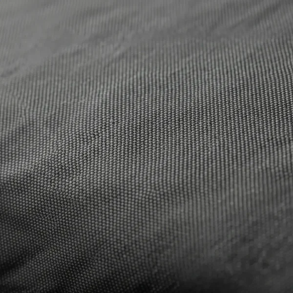Extreme closeup of a dark grey nylon softshell fabric, showing the tight, durable woven texture and slight sheen.